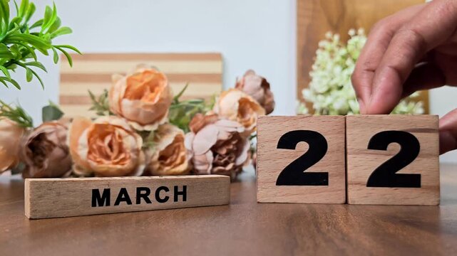 Hand placing wooden calendar blocks showing march 22 on a wooden table