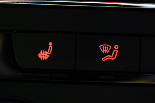 Close up of car dashboard buttons featuring illuminated red icons for seat heating and windshield climate ventilation.