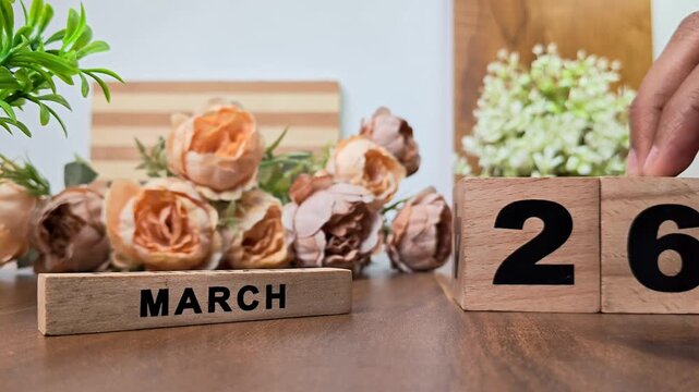 Hand placing wooden calendar blocks showing march 26 on a wooden table