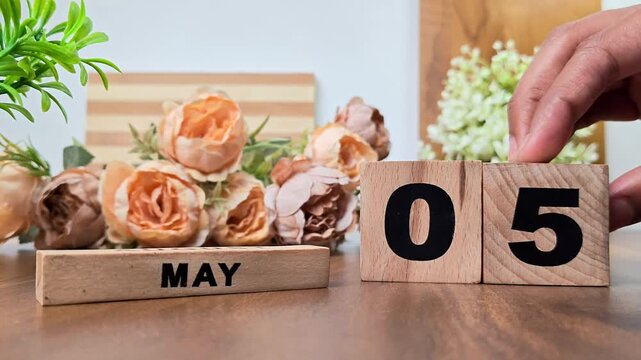 Hand placing wooden calendar blocks showing may 5 on a wooden table