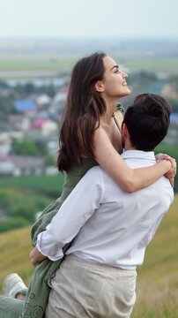 Passionate young couple enjoying a romantic moment outdoors on a scenic hillside, with a strong man lovingly lifting and spinning his beautiful laughing girlfriend in his arms