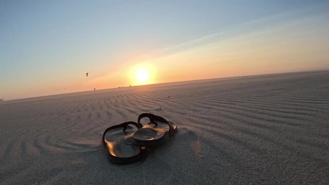 Peaceful beach scene with flip-flops on Kijkduin Beach as kitesurfers glide across the sea at sunset