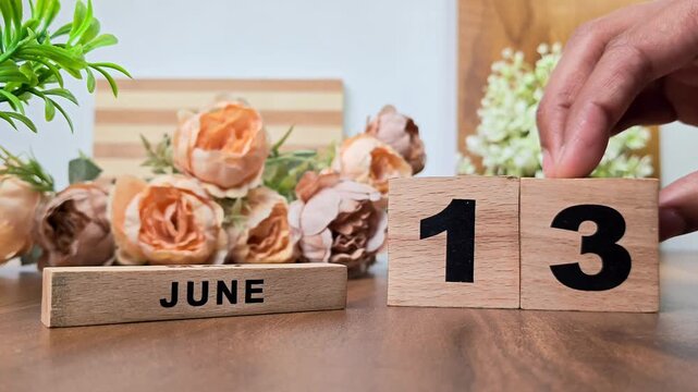 Hand placing wooden calendar blocks showing june 13 on a wooden table