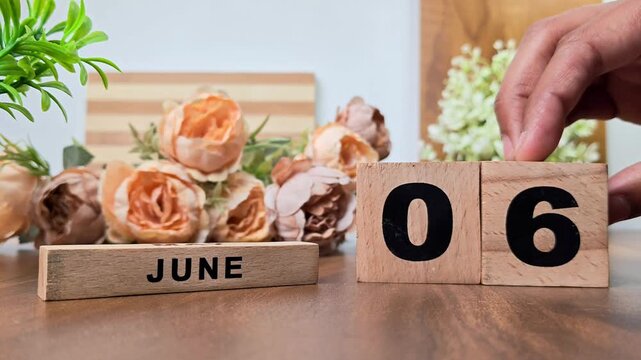 Hand placing wooden calendar blocks showing june 6 on a wooden table