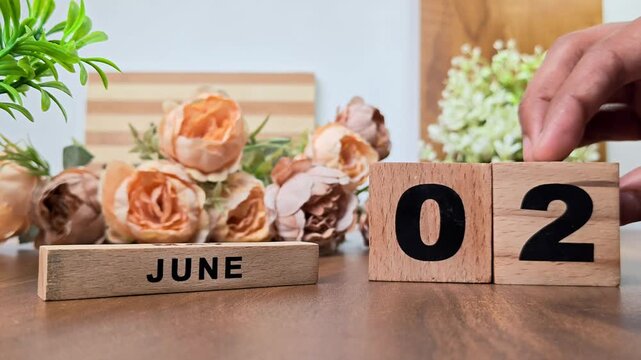 Hand placing wooden calendar blocks showing june 2 on a wooden table