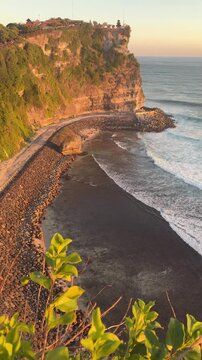 A scenic view of a rocky beach with waves crashing against the shore. Lush green foliage frames the scene, highlighting the natural beauty of the coastline.