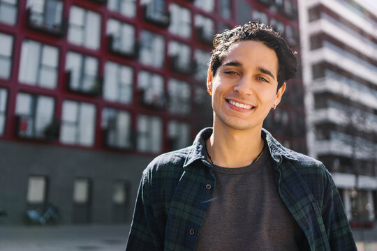 Content young hispanic man portrait outdoors in modern urban city looking to camera with positive smile