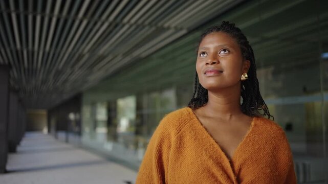 Pensive African American elegant woman standing and thinking in a modern glass building