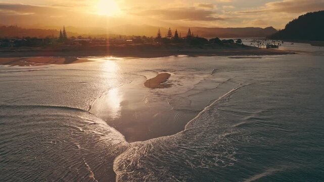 Aerial view of the serene Whangamata harbour and sandy beach at sunset in the Coromandel Peninsula, New Zealand, with warm golden reflections.