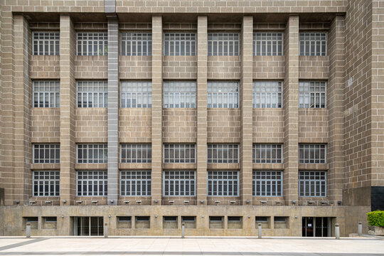 A symmetrical exterior view of a historic or classic stone building facade featuring a structured grid of windows, stone pillars, and architectural details, urban architecture concept.