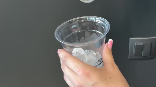 Scooping ice cubes into plastic takeaway cup with ice scoop, drink preparation for cold beverages and cocktails on gray background close up