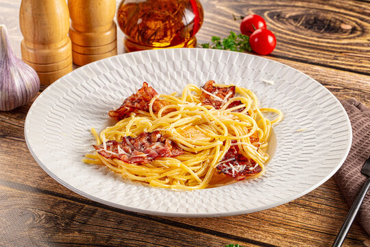 Spaghetti carbonara with crispy bacon and parmesan cheese on rustic wooden table