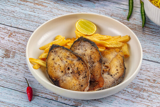 Pan fried kingfish steaks with french fries and lime garnish in white bowl on rustic wooden table
