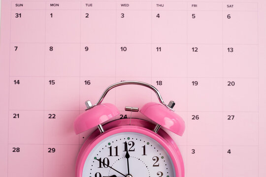 Pink alarm clock on a pink monthly calendar planner for deadline and time management concept
