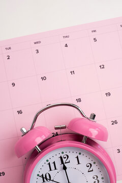 Pink alarm clock on a pink monthly calendar planner for deadline and time management concept