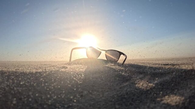 Peaceful beach atmosphere with sunglasses in the foreground and kitesurfers enjoying strong coastal winds at sunset