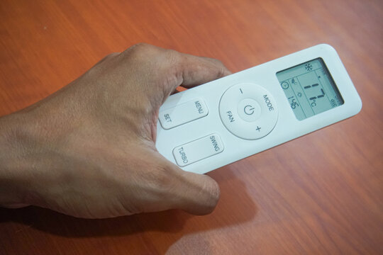 Person Holding White Air Conditioner Remote Controller On Wooden Table