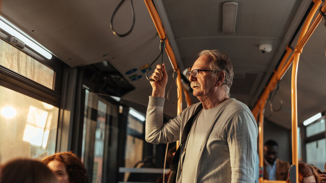 Senior man standing in bus using handrail