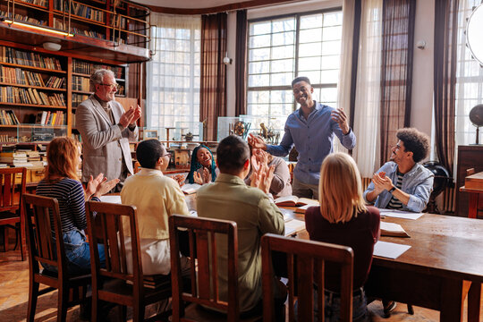 Diverse students applauding male presenter in library