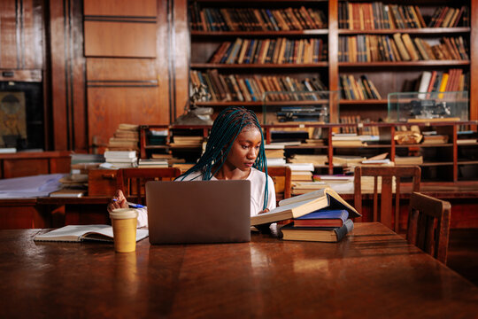 Female student studying with books and laptop in library