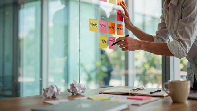 Business strategy session man brainstorming ideas on glass wall with sticky notes and pen