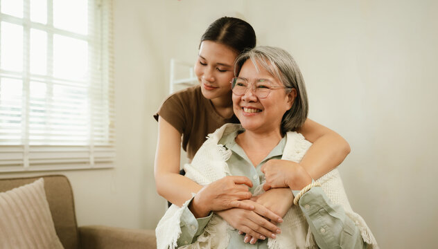 Young caregiver warmly hugging a smiling senior woman at home, expressing love, comfort, trust, and compassionate elderly care.