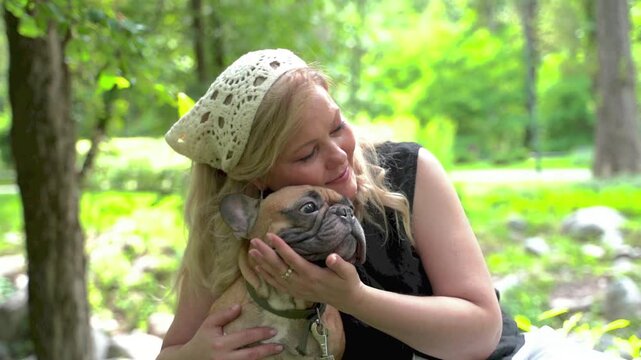 Woman hugging and cuddling French bulldog in park with love and affection