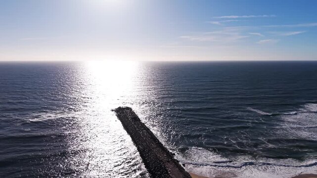 Aerial - Stone breakwater extending into ocean at sunset