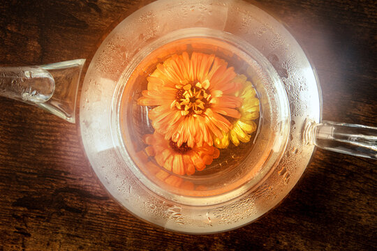 Fresh calendula herbal tea in a glass teapot, a flat lay