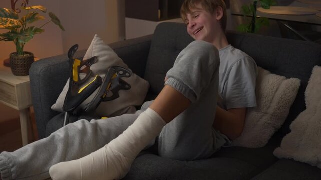Teenage boy reading a book while recovering at home with his injured leg bandaged. Education, learning, literature, personal development and productive leisure time concept.