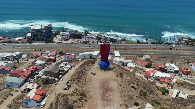 Drone establishing shot behind Christ of the Sacred Heart monument overlooking Rosarito coastal city and the Pacific coast
