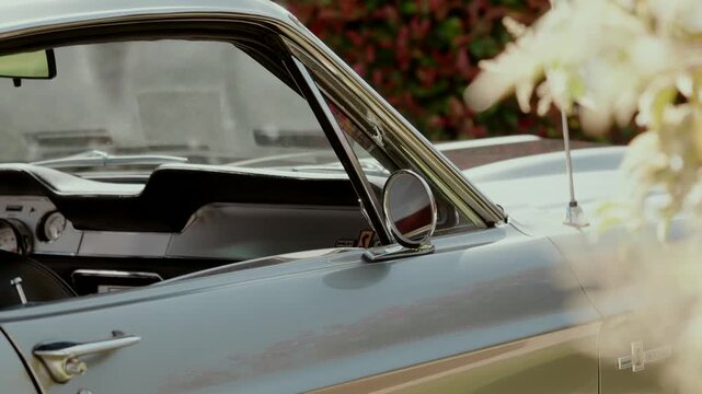 Classic car window side mirror and door handle beside white flowers