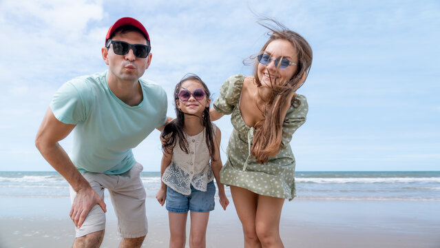 Parents show affection to their daughter beside the sea creating an authentic lifestyle image that represents family unity care support and joyful childhood.
