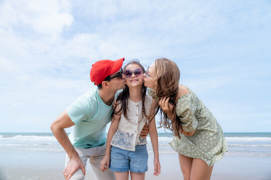 Loving parents kiss their smiling daughter on a beautiful beach celebrating family affection childhood happiness emotional bonding and unforgettable summer vacation memories.
