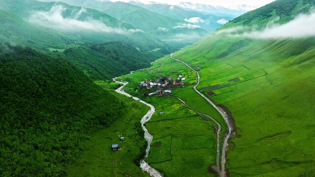 Serene mountain village nestled in lush green valley with winding river aerial drone footage.