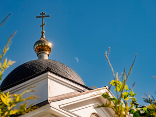 Golden cross and dome of an Orthodox church against a clear blue sky with a crescent moon © LemPro Filming Life