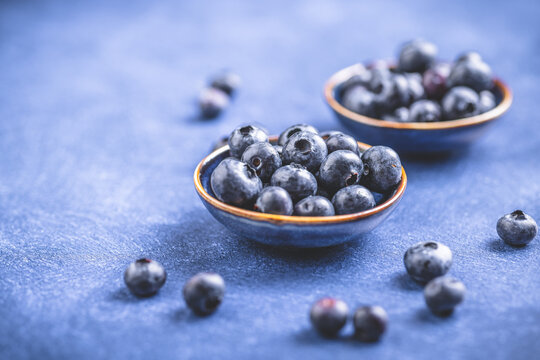 Organic fresh blueberries served in small bowls on a textured blue surface