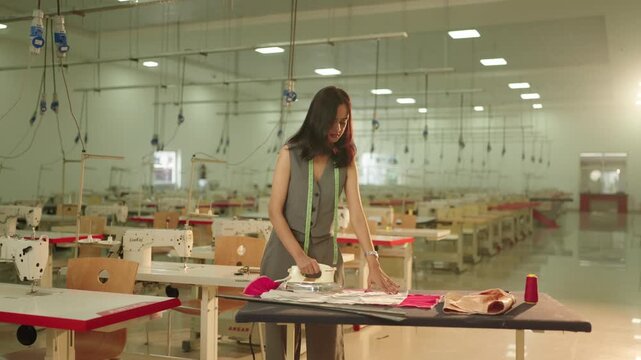 Focused fashion student operating industrial sewing machine guiding fabric carefully under needle in bright design workshop setting