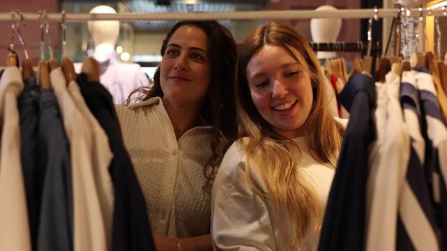 Two cheerful female friends enjoying their time together while choosing new outfits in a fashion store