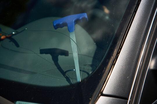 Windshield Replacement and Removal. Service worker pulls cutting wire through adhesive layer under broken auto glass. Technician performs car window extraction in professional repair garage