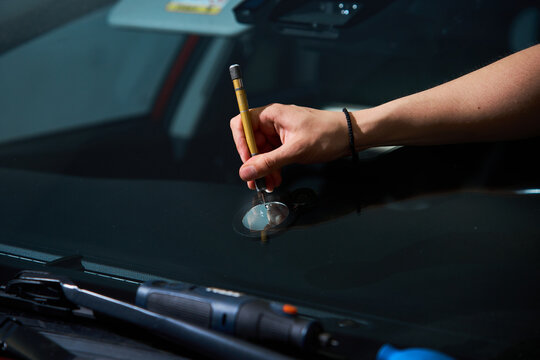 Windshield repair service. Expert mechanic prepares glass damage for treatment using specialized scriber tool. Technician uses precision scriber to clean glass damage point