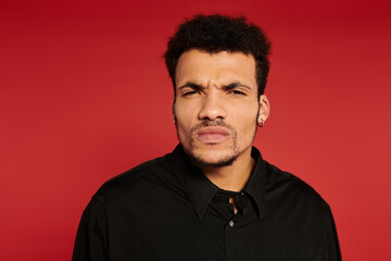Fototapeta premium A young man with stylish hair and a serious expression stands against a bright red background.