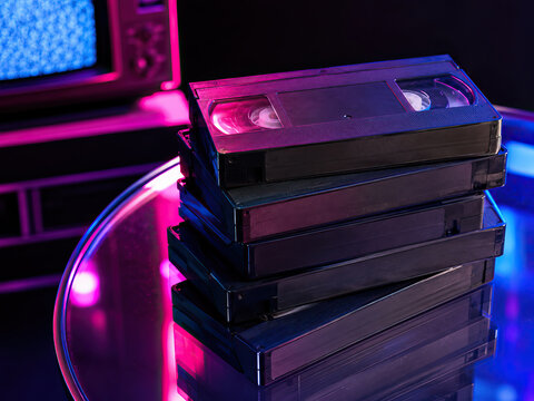 A stack of vintage VHS tapes with a reflective surface, showcasing the material and subtle wear, set against a blurred television screen displaying blue static.