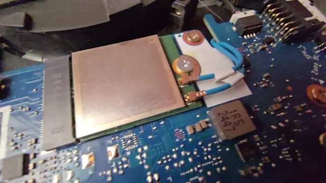 Close-up macro video footage showing internal computer components, including speaker and backlight cable connectors, microchips, and a wireless network Wi-Fi card mounted on a blue motherboard PCB. 