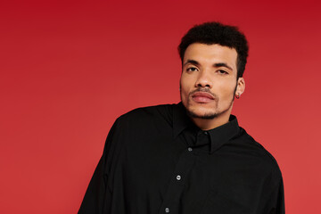 Obraz premium A black man, handsome man stands confidently with a slight tilt against a vivid red backdrop.