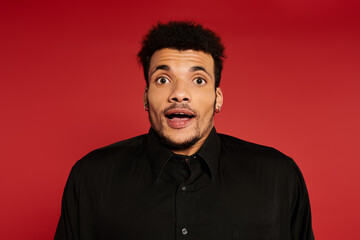 Obraz premium A young handsome man shows a surprised expression while posing against a bright red background.