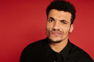 Obraz premium A young handsome man displays a playful expression against a vibrant red backdrop.