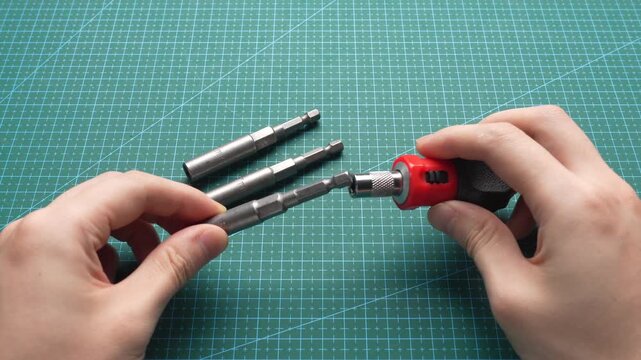 Close-up of hands inserting hex bit adapter into red-and-black torque screwdriver on green cutting mat