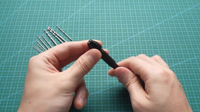 Close-up of hands adjusting a mini hand drill chuck with precision drill bits on green cutting mat