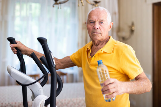 Elderly sporty man exercising on an elliptical trainer and drinking water from bottle